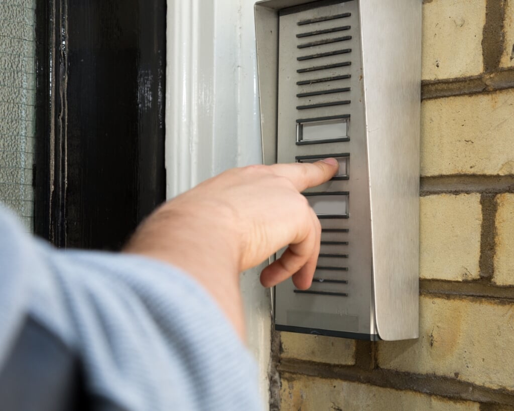 Close up view of the hand of a man ringing an intercom to gain access to an apartment building or business premises, wall-mounted on brickwork