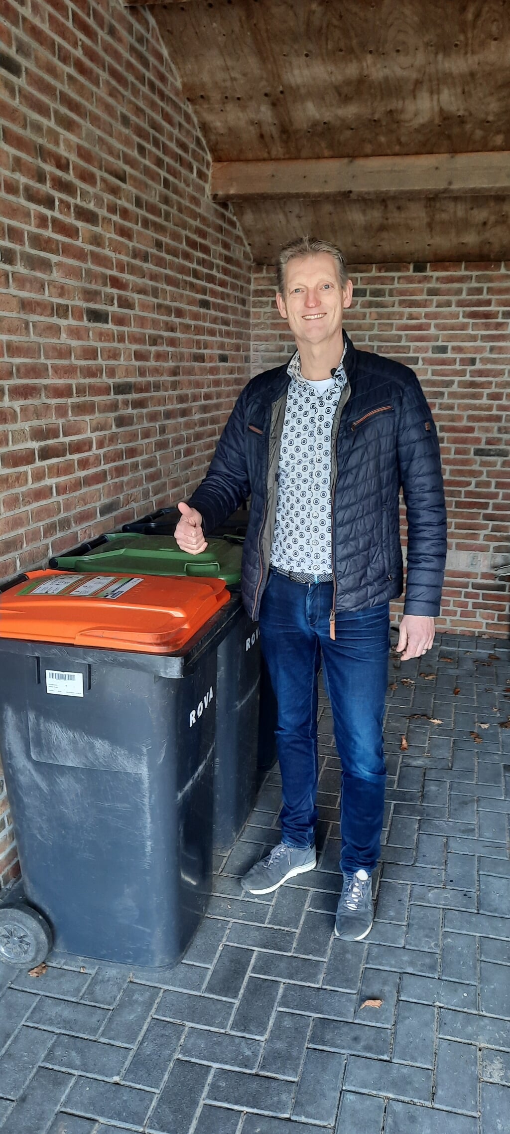 Wethouder Erik Volmerink plakt zelf een sticker op zijn afvalcontainer, die net buiten beeld staat in deze verticale foto.