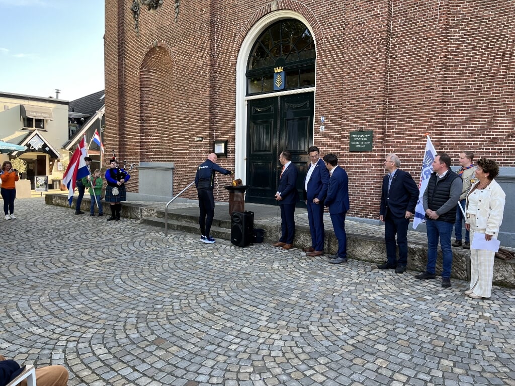 Atleet Hans ter Steege steekt het bevrijdingsvuur aan voor de Schildkerk. Rechts de wethouders René de Koff, Bert Tijhof en Erik Wessels.