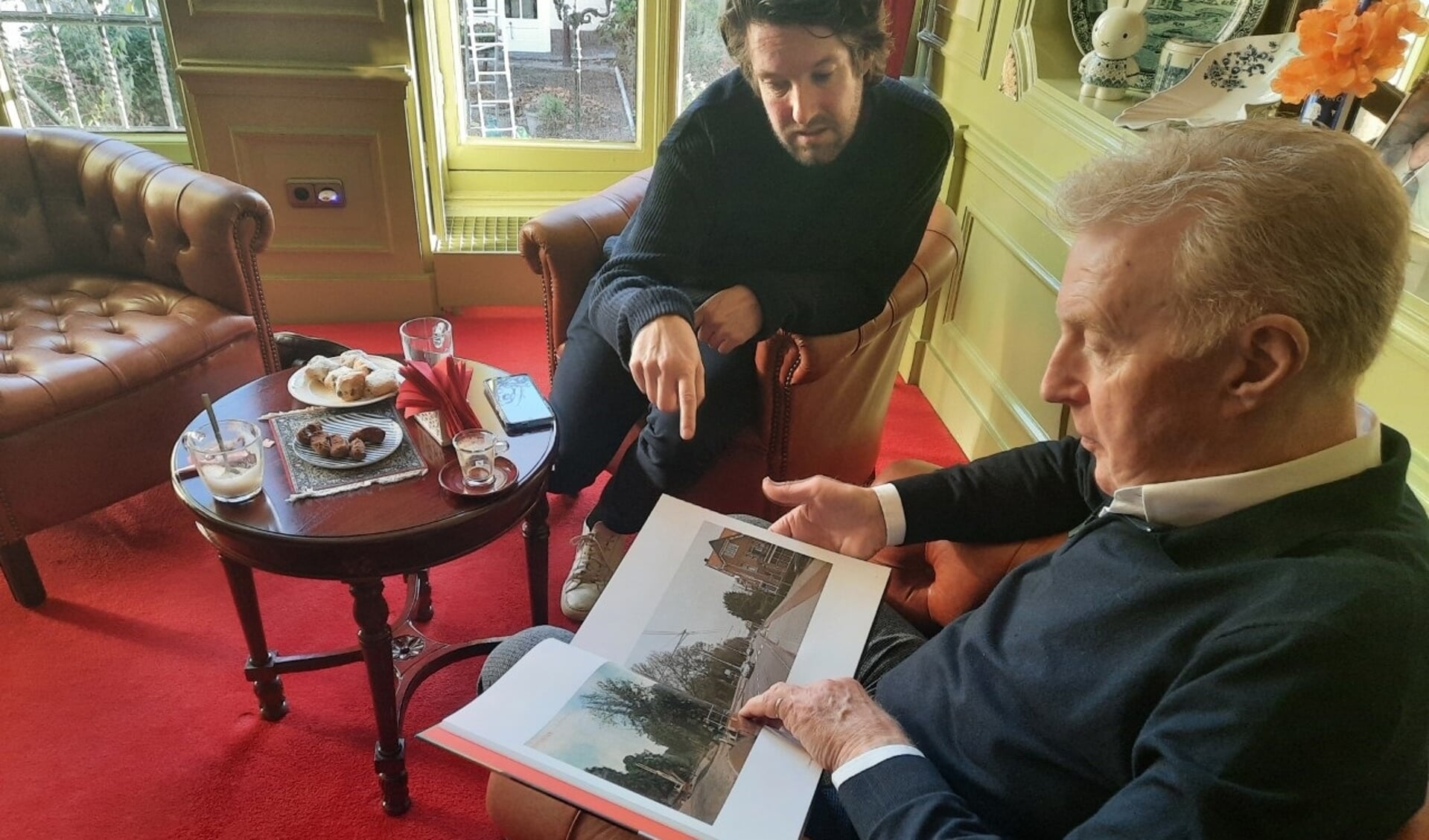 André van Duin bladert met onze verslaggever Peter van Drunen door het boek ‘Groeten uit Rotterdam’ met foto’s van nu en honderd jaar geleden. “Kijk, dit is Delfshaven. Hier heb ik veel gespeeld.” Foto: Rico Hop