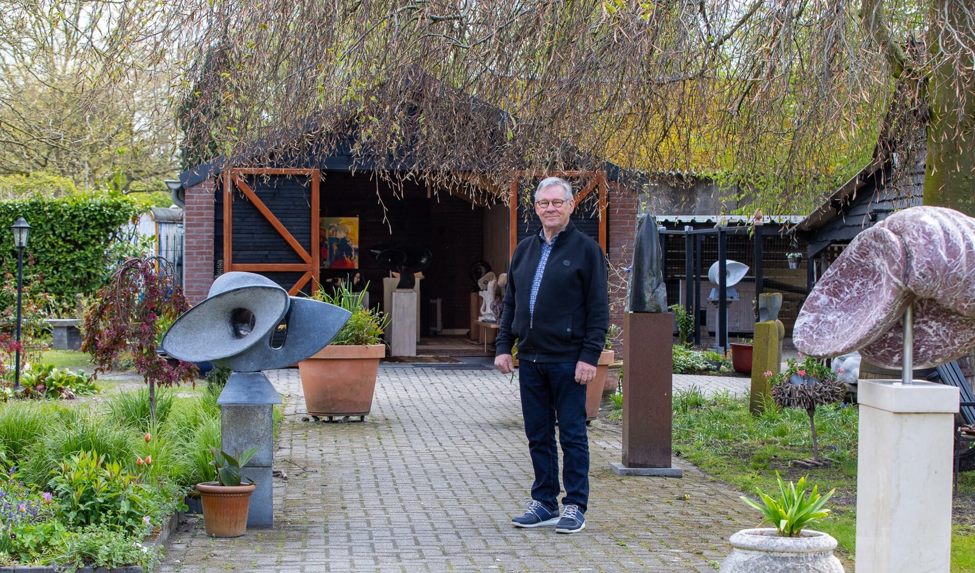 Cees Meijer in zijn beeldentuin. Op de achtergrond zijn atelier.