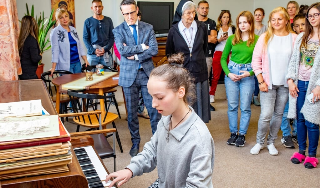 Een jong Oekraïens meisje speelt een stukje op de piano onder het toeziend oog van haar landgenoten, de burgemeester en Zr. Marie Benedicte