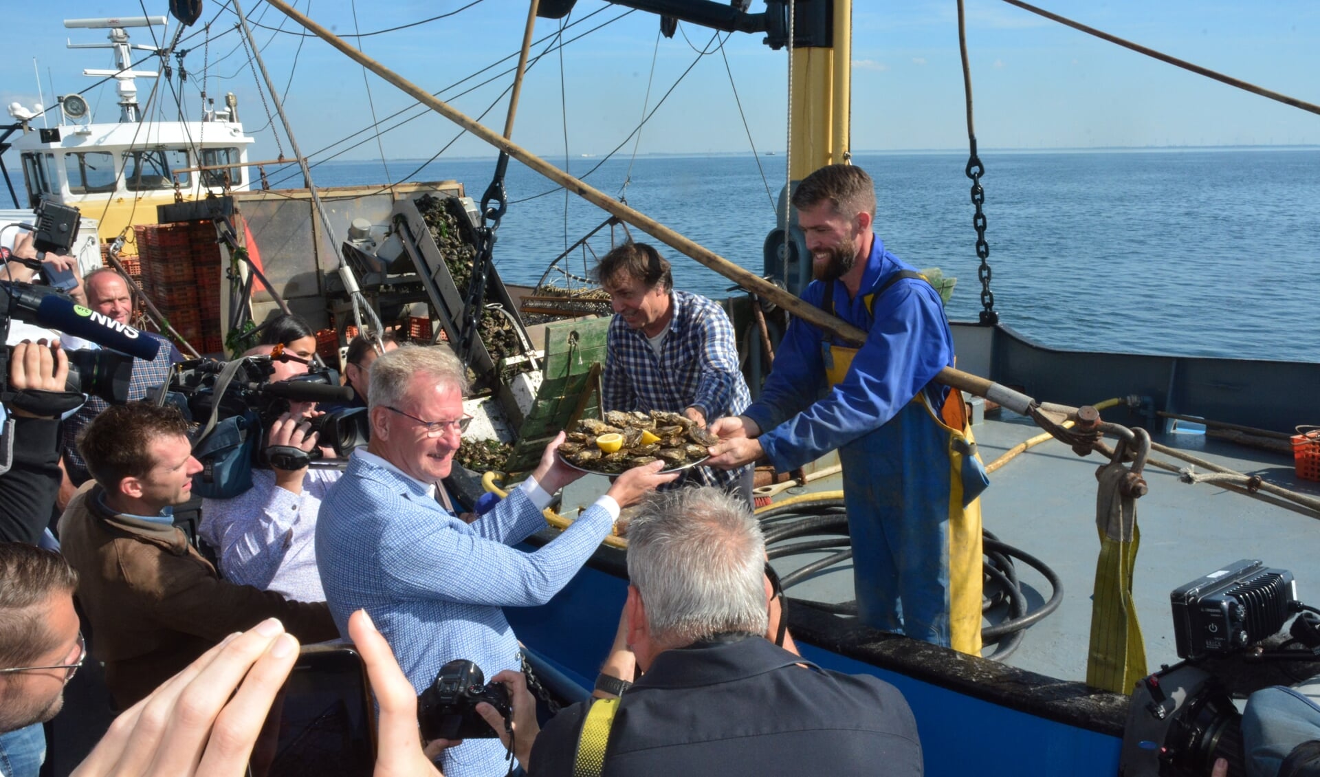 H Omgeven door het journaille neemt Kees van Beveren de eerste oesters in ontvangst van schipper-eigenaar Adri Sinke (YE 147) en  opvarende Luuk Sinke. 