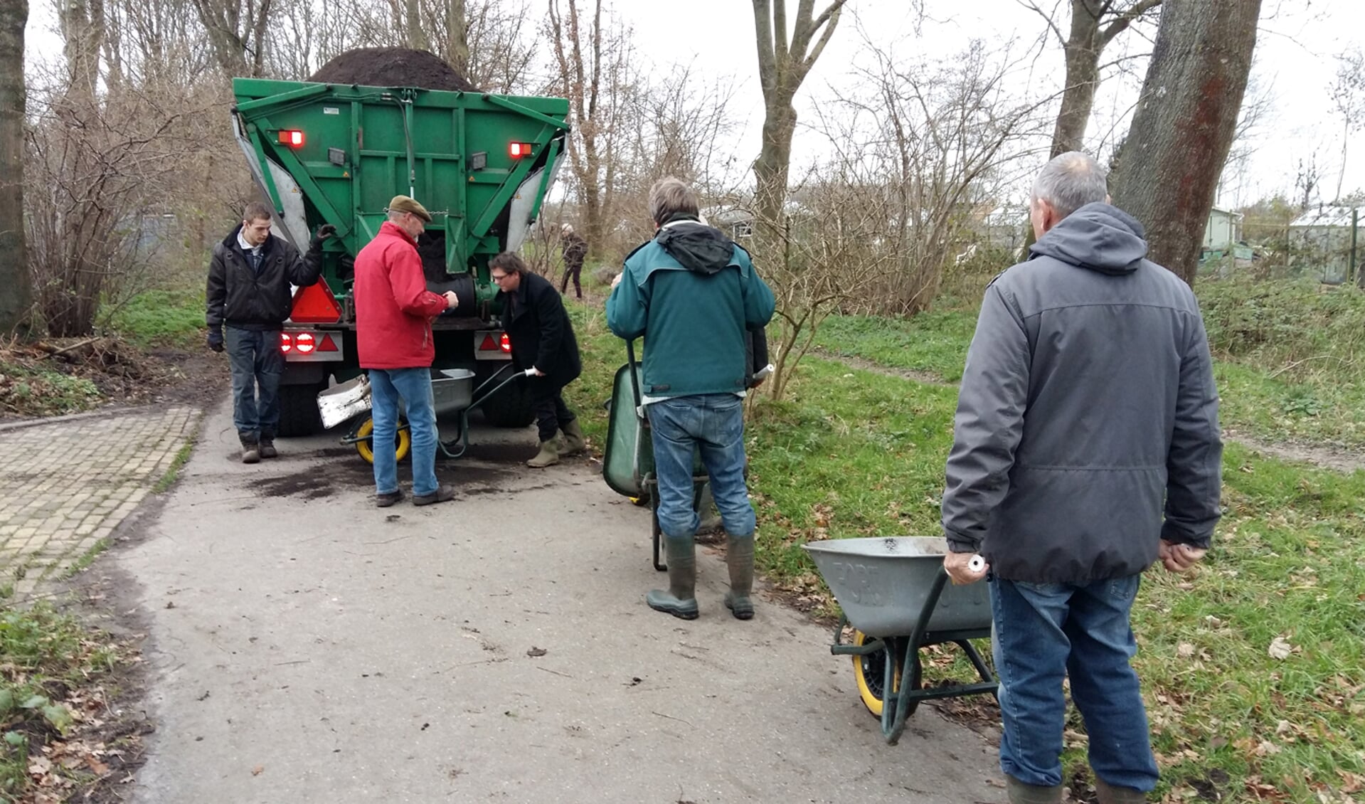 Vrijwilligers van de schooltuinen halen kruiwagen na kruiwagen compost die vervolgens over de tuinen wordt uitgespreid. | Foto: PR