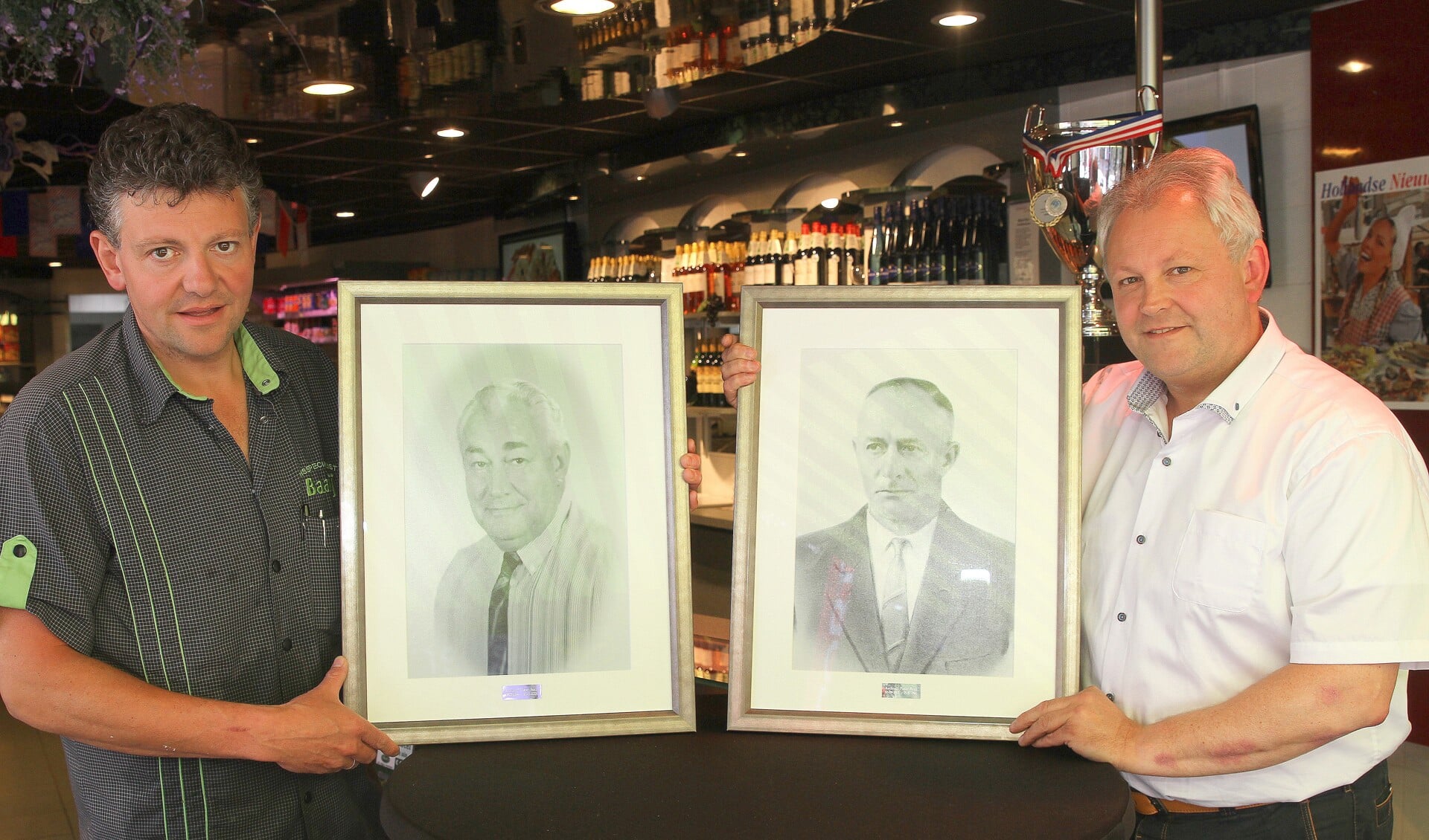 Kees (links) en Ad Baaij met de grondleggers van het bedrijf: hun opa Toon (fotolijst rechts) en vader Toon (lijst links). | Foto: Arie in 't Veld