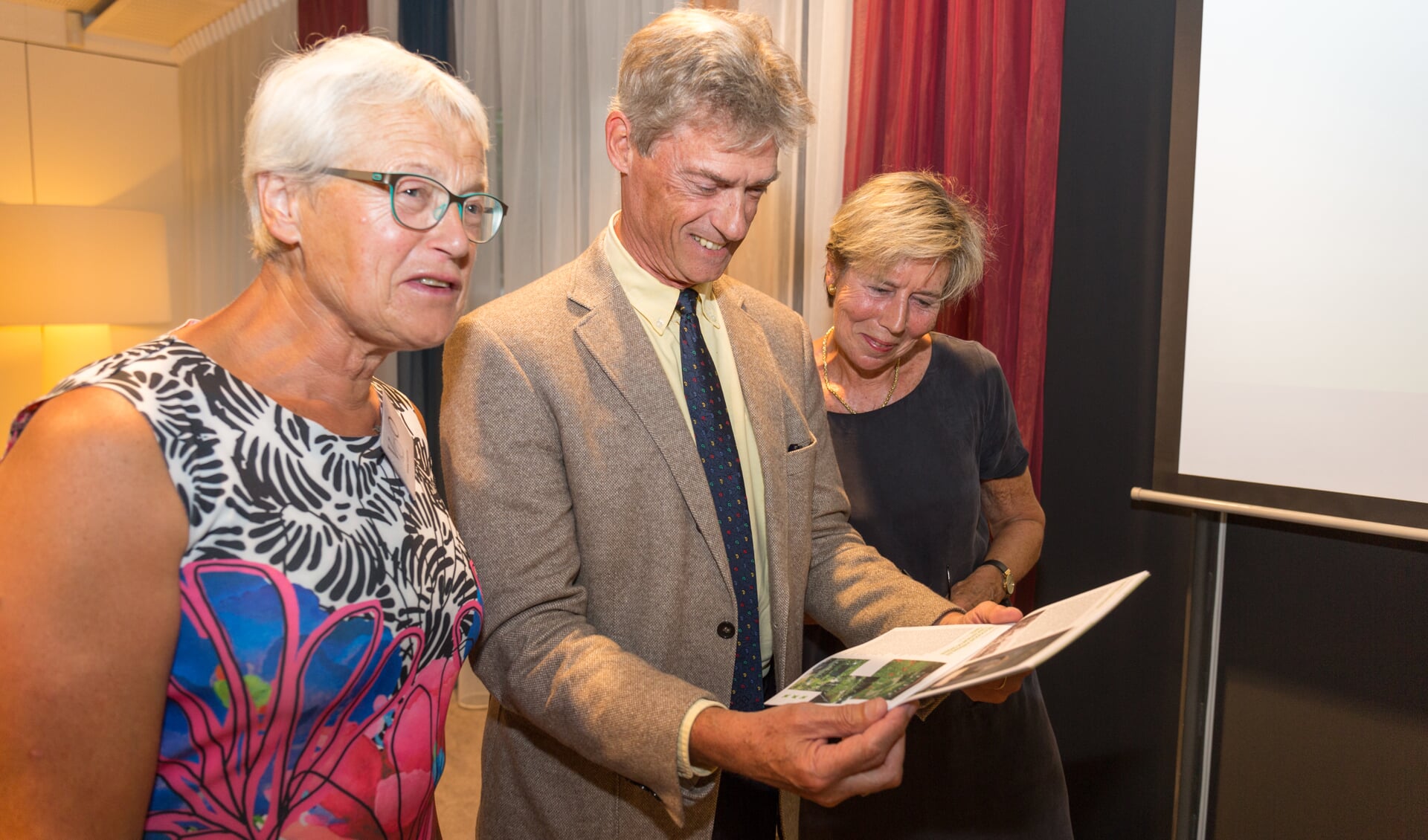 Wethouder Roeffen bewondert het programmaboekje geflankeerd door de twee voorzitters. | Foto Wil van Elk