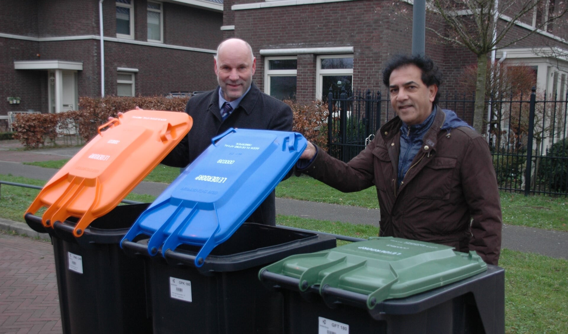 Wethouder McDaniel (links) heeft de eerste set minicontainers overhandigd aan bewoner Rob Mohanlal. De groene container is voor GTF, de blauwe voor papier en de oranje voor PMD. 