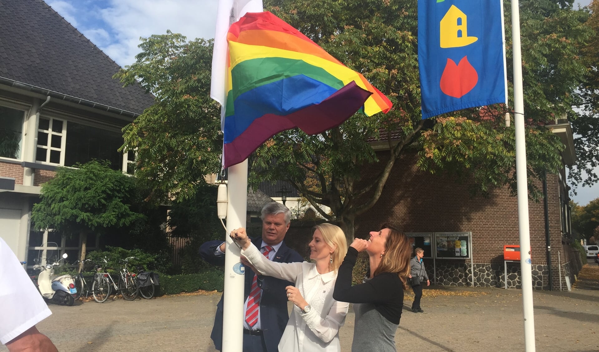Wethouders Kees van der Zwet, Jeanet van der Laan en Jolanda Langeveld hijsen de blanco en de regenboogvlag.