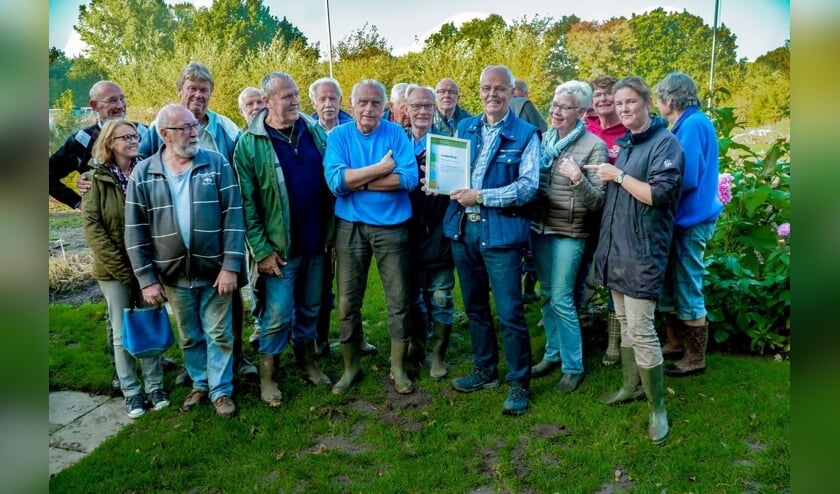 Voorzitter Joop van Huut van de schooltuinen toont de oorkonde, om hem heen staan de onmisbare vrijwilligers van schooltuinencomplex De Sterrekers.