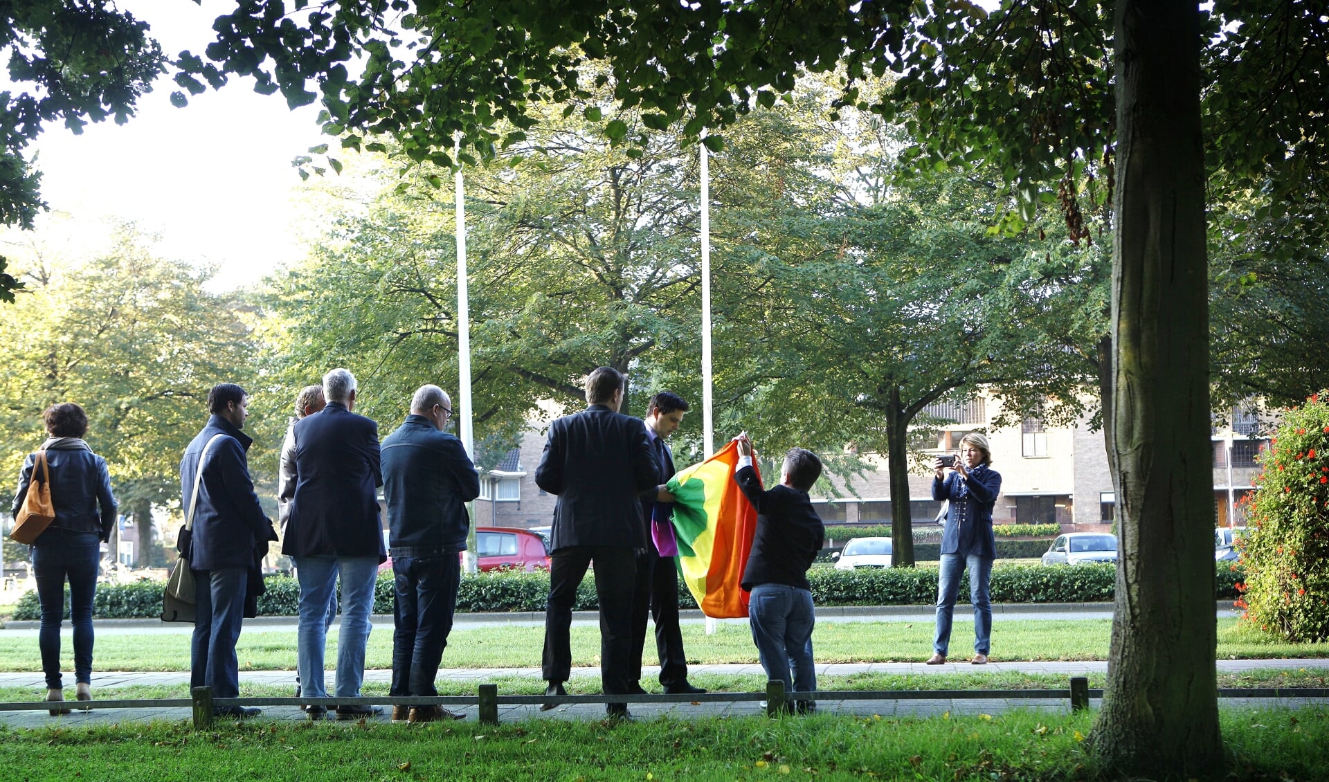 Raadsleden en COC-leden bij het hijsen van de regenboogvlag in de mast tegenover het gemeentehuis.