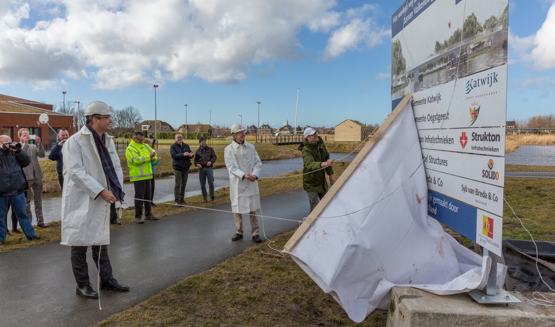 De harde wind plaagde de wethouders bij het onthullen van het bouwbord. | Foto Wil van Elk