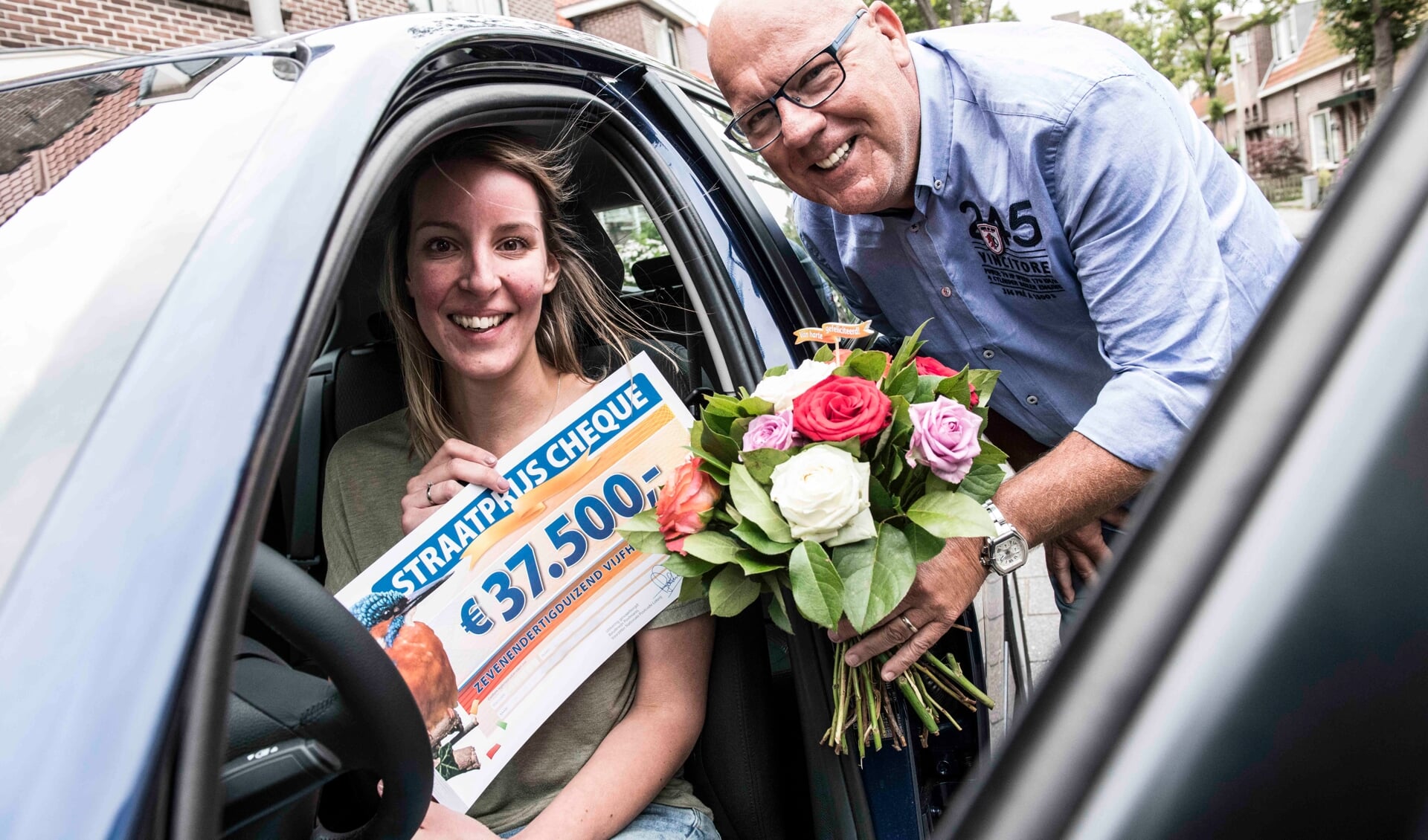 Liesbeth wordt verrast door Postcode Loterij-ambassadeur Gaston Starreveld met de PostcodeStraatprijs-cheque en de BMW. | Foto Jurgen Jacob Lodder