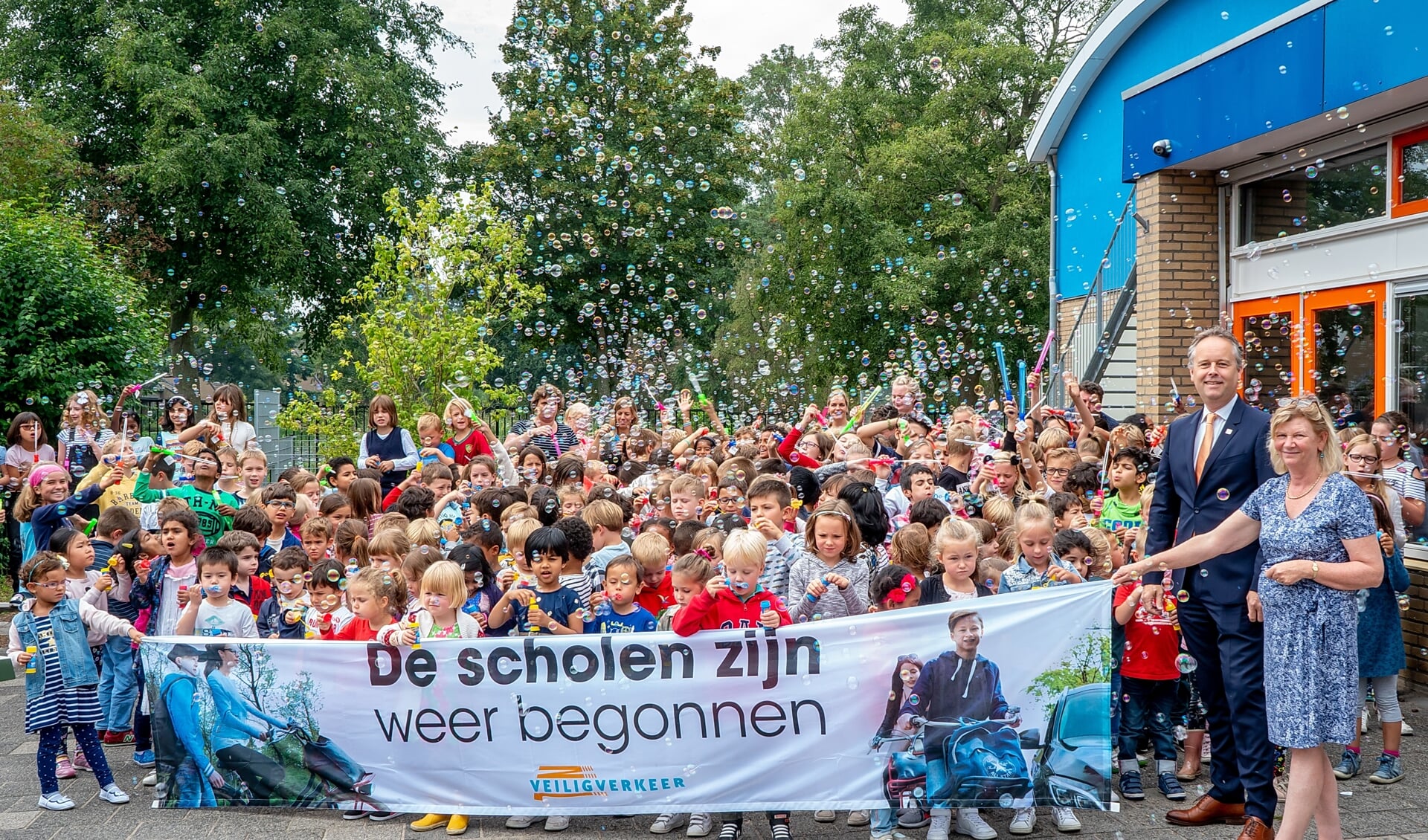 Allemaal bellen blazen om aandacht te vragen voor de campagne 'De scholen zijn weer begonnen'. Rechts naast het spandoek staat wethouder Willem Joosten. 