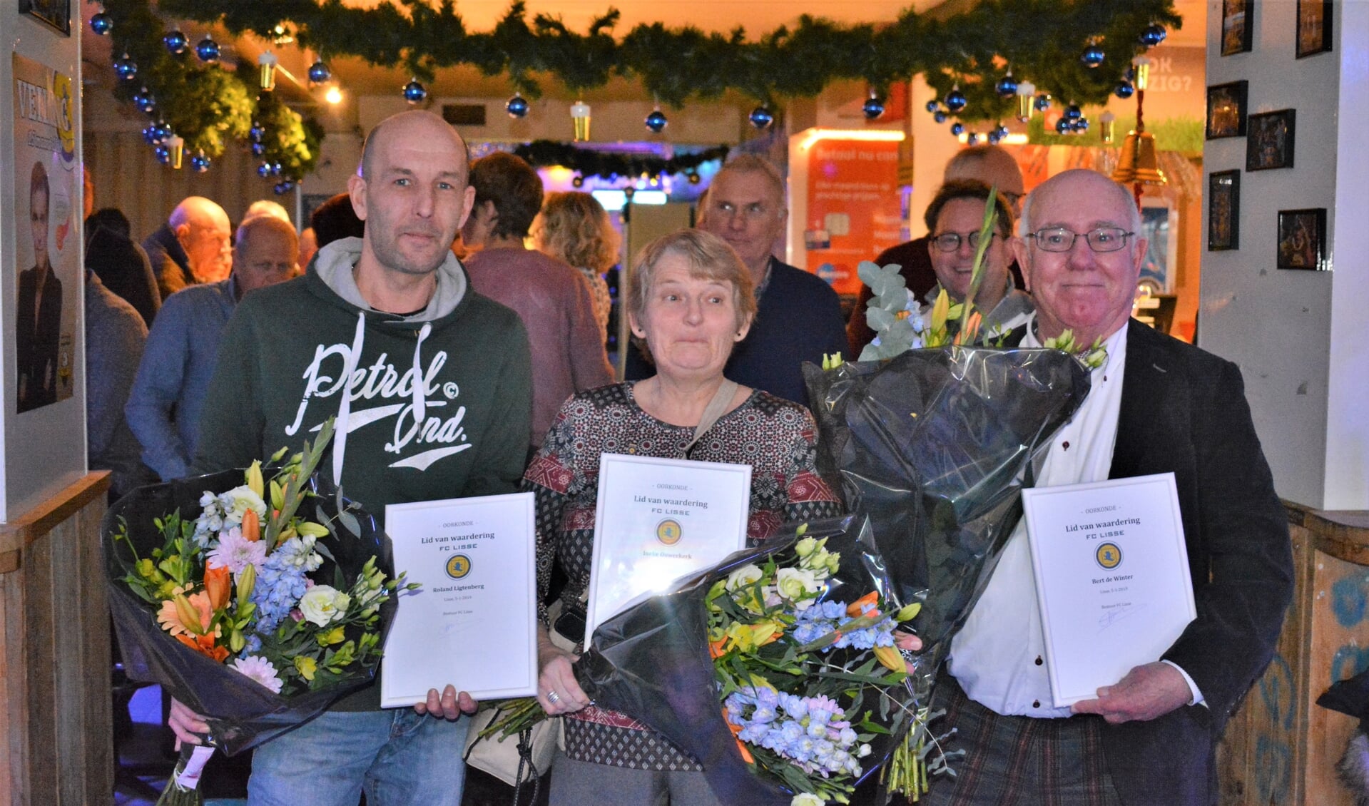 Roland, Ineke en Bert met bloemen en de waarderingsspeld voor hun vrijwilligerswerk.