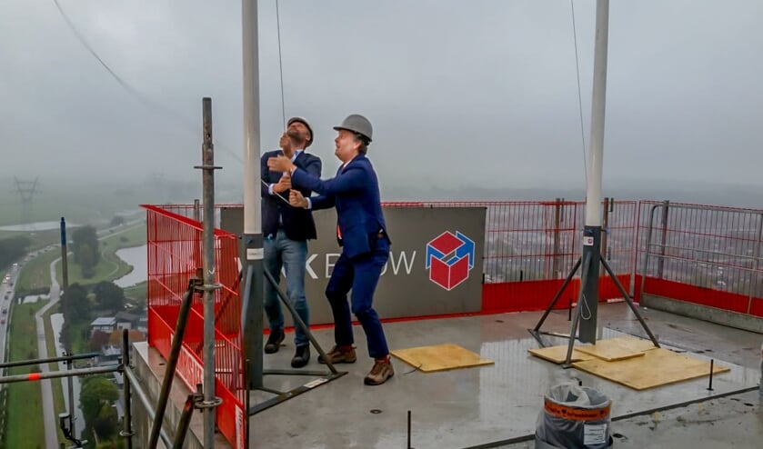Bernlef de Vries van Vink Bouw (links) en wethouder Willem Joosten hijsen de vlag; het hoogste punt van de torenflat is bereikt.