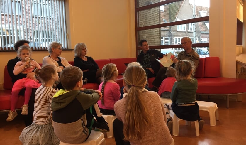 Ed Hoogkamer (met boek) leest voor, terwijl naast hem Paul Zwetsloot, samen met de kinderen, toeluistert.