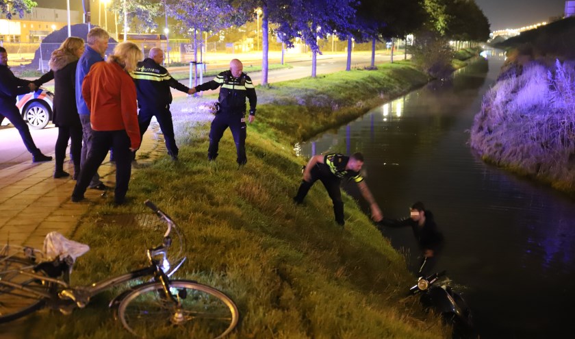 Een politieman helpt de beschonken scooterrijder op de kant.
