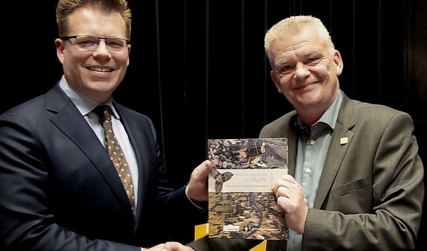 Menno Dijkstra (links) overhandigt het eerste exemplaar van het publieksboekje 'Nieuw Licht op Leython' aan wethouder Daan Binnendijk.