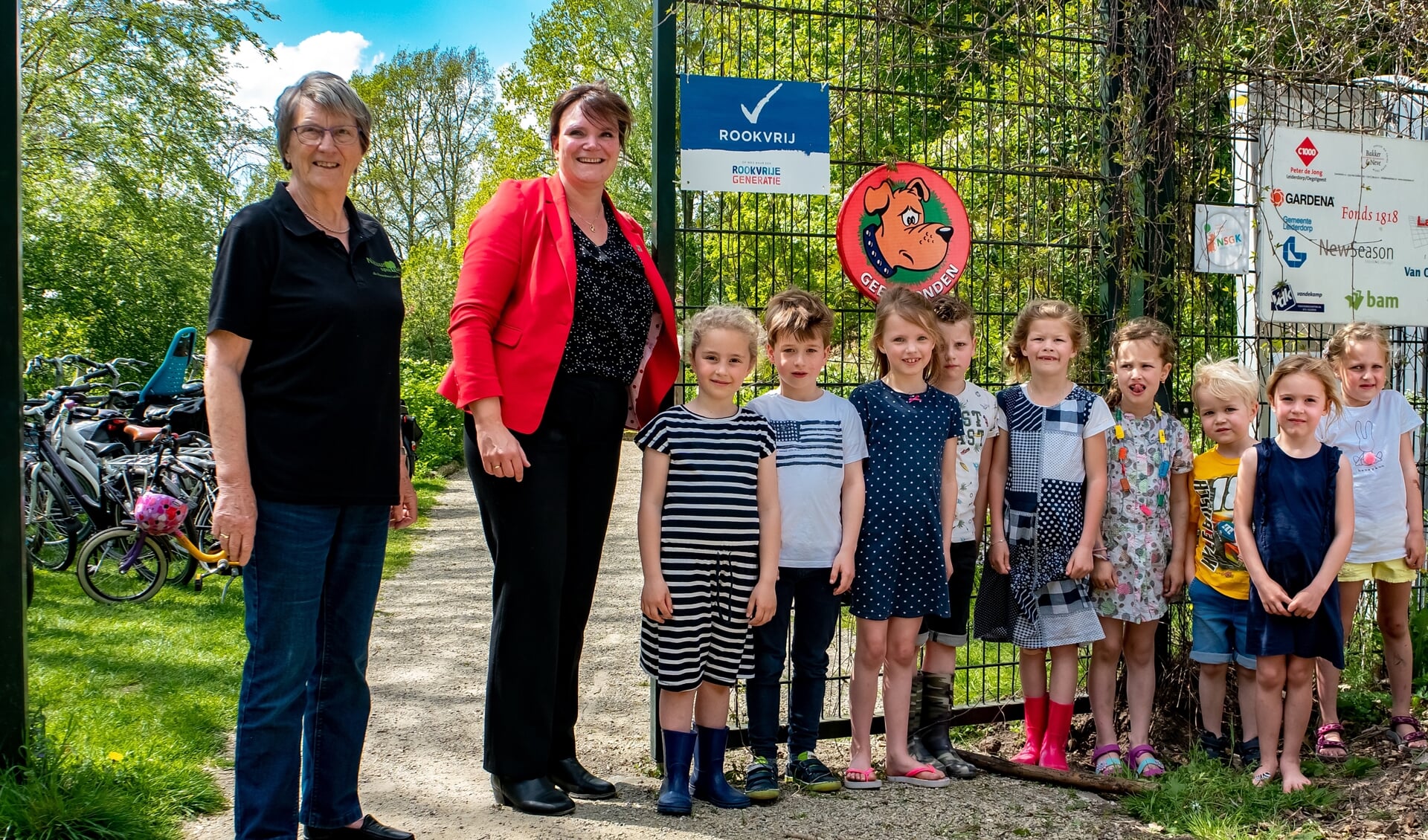 Wethouder Angelique Beekhuizen (met rood jasje) heeft, onder toeziend oog van een groep speeltuingebruikertjes, het bord 'Rookvrij' onthuld. Links voorzitter Riny Vons van de Stichting Natuurspeeltuin Leiderdorp.