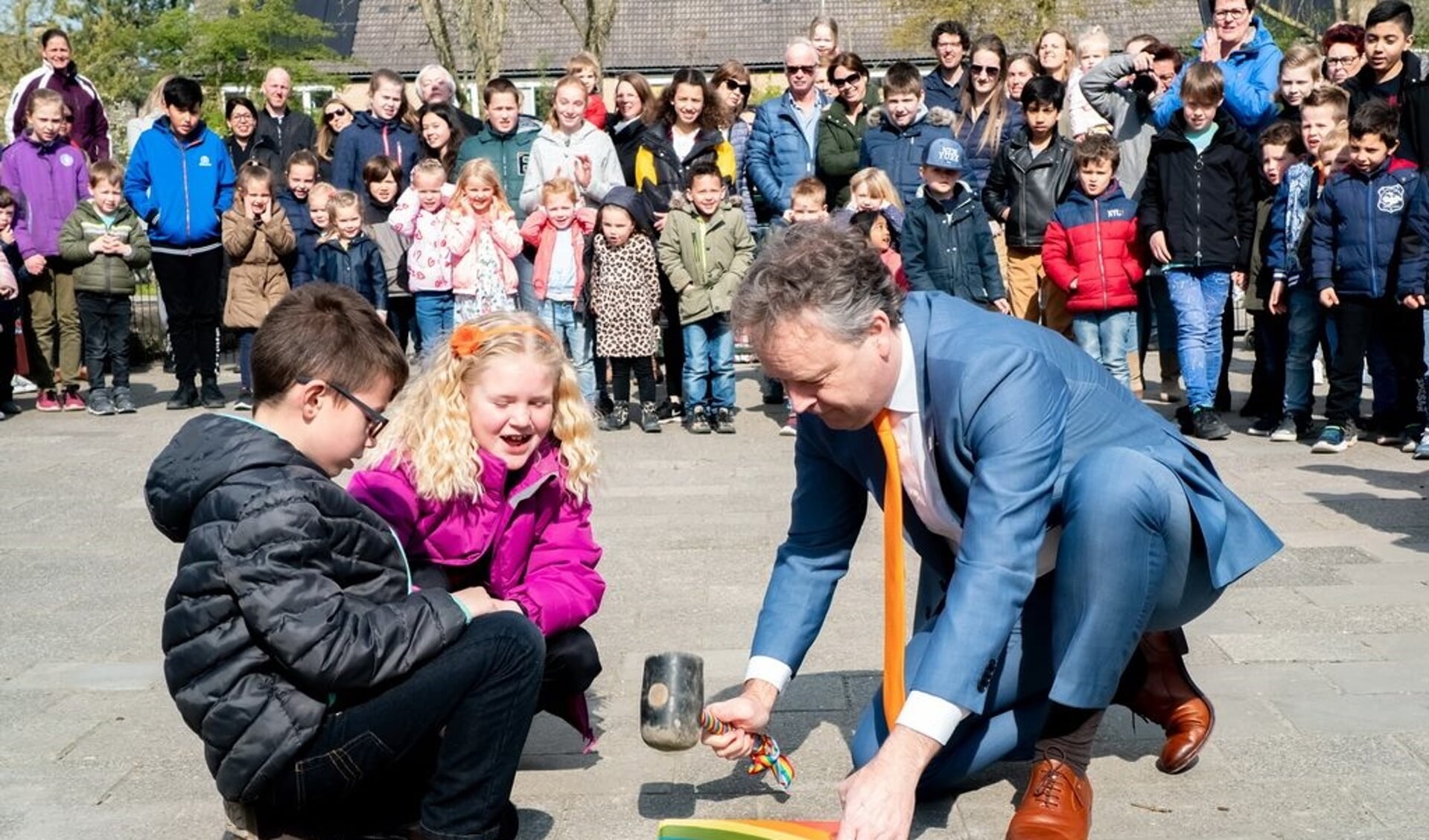 Samen met twee leerlingen legt wethouder Willem Joosten de laatste steen in het vernieuwde plein van PCOB De Regenboog. 