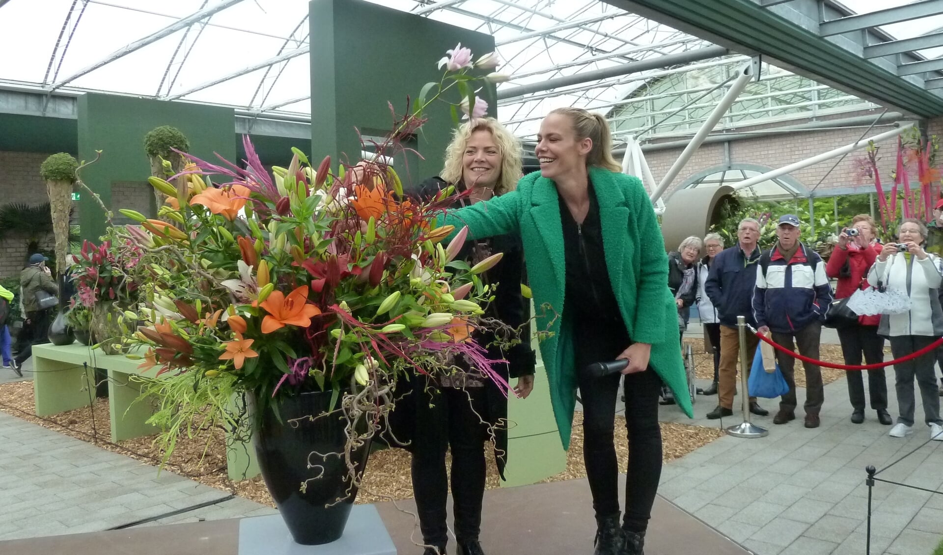 Nicolette Kluijver (rechts) steekt een lelietak in een bloemstuk, daarbij bijgestaan door Stephanie van Erven.