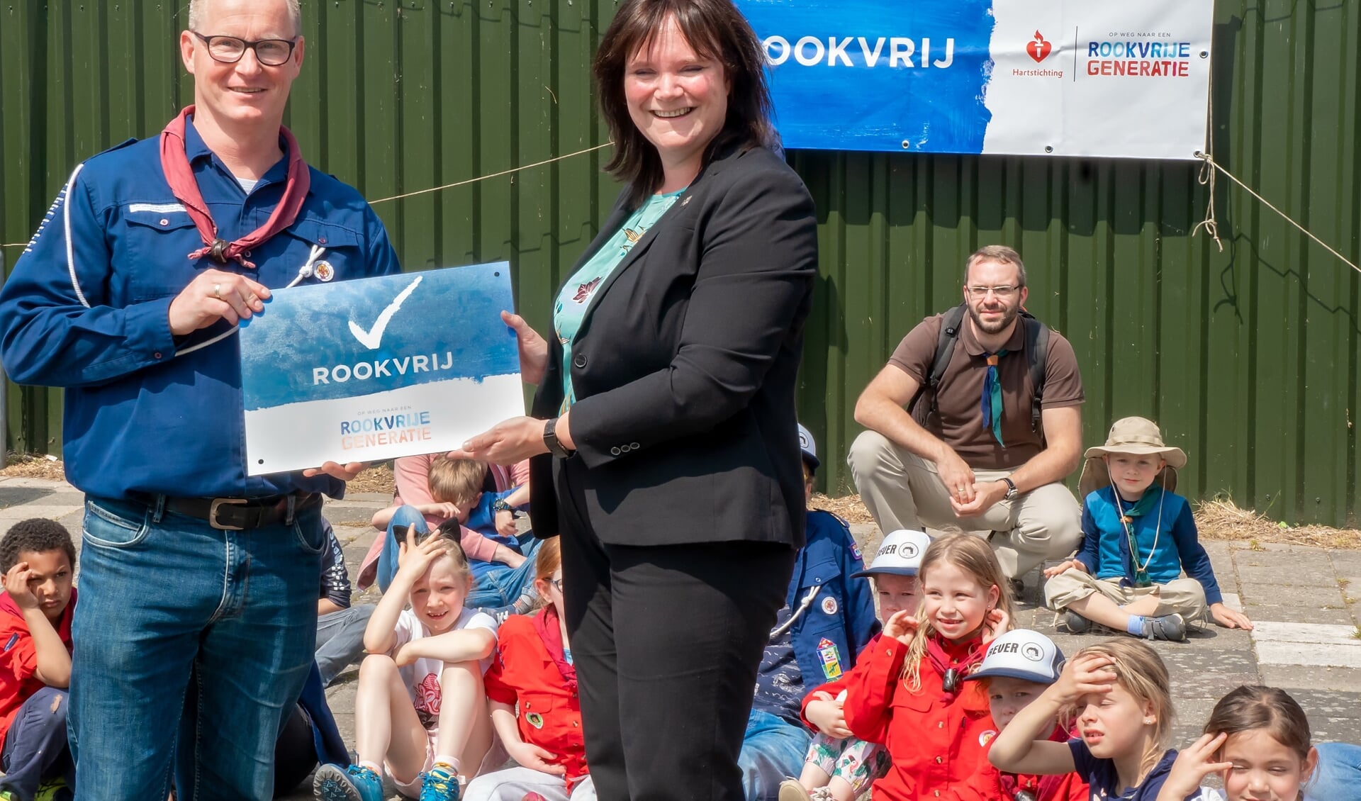 Wethouder Angelique Beekhuizen overhandigt het bord ‘Rookvrij’ aan voorzitter Bas van den Berg van de scoutingvereniging.