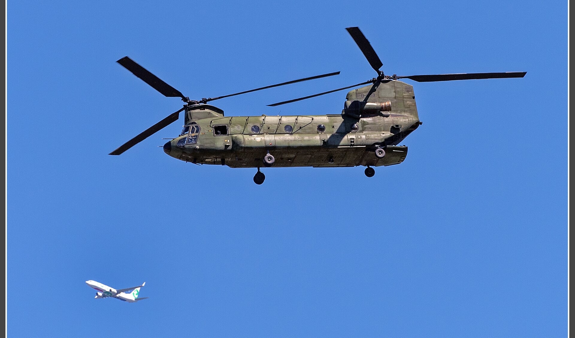 Een chinook transporthelikopter met zijn dubbele rotors. Op de achtergrond een Transavia lijnvliegtuig.