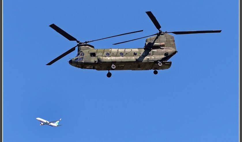 Een chinook transporthelikopter met zijn dubbele rotors. Op de achtergrond een Transavia lijnvliegtuig.