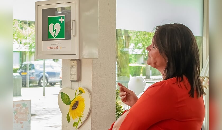 Wethouder Beekhuizen onthult de AED. Onder het apparaat een beschilderd hart, gemaakt door een 86-jarige bezoeker van 't Buurthuis.