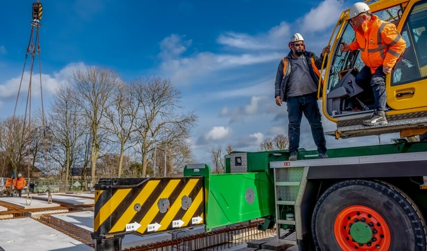 Wethouder Rik van Woudenberg (met oranje jas) heeft net het officiële eerste brugdeel op zijn plek gelegd.