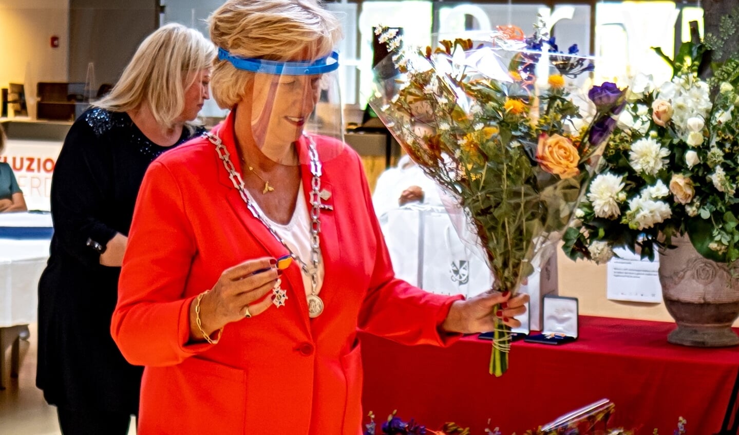 Burgemeester Laila Driessen met lintje en bloemen én getooid met spatmasker op weg naar één van de gedecoreerden.