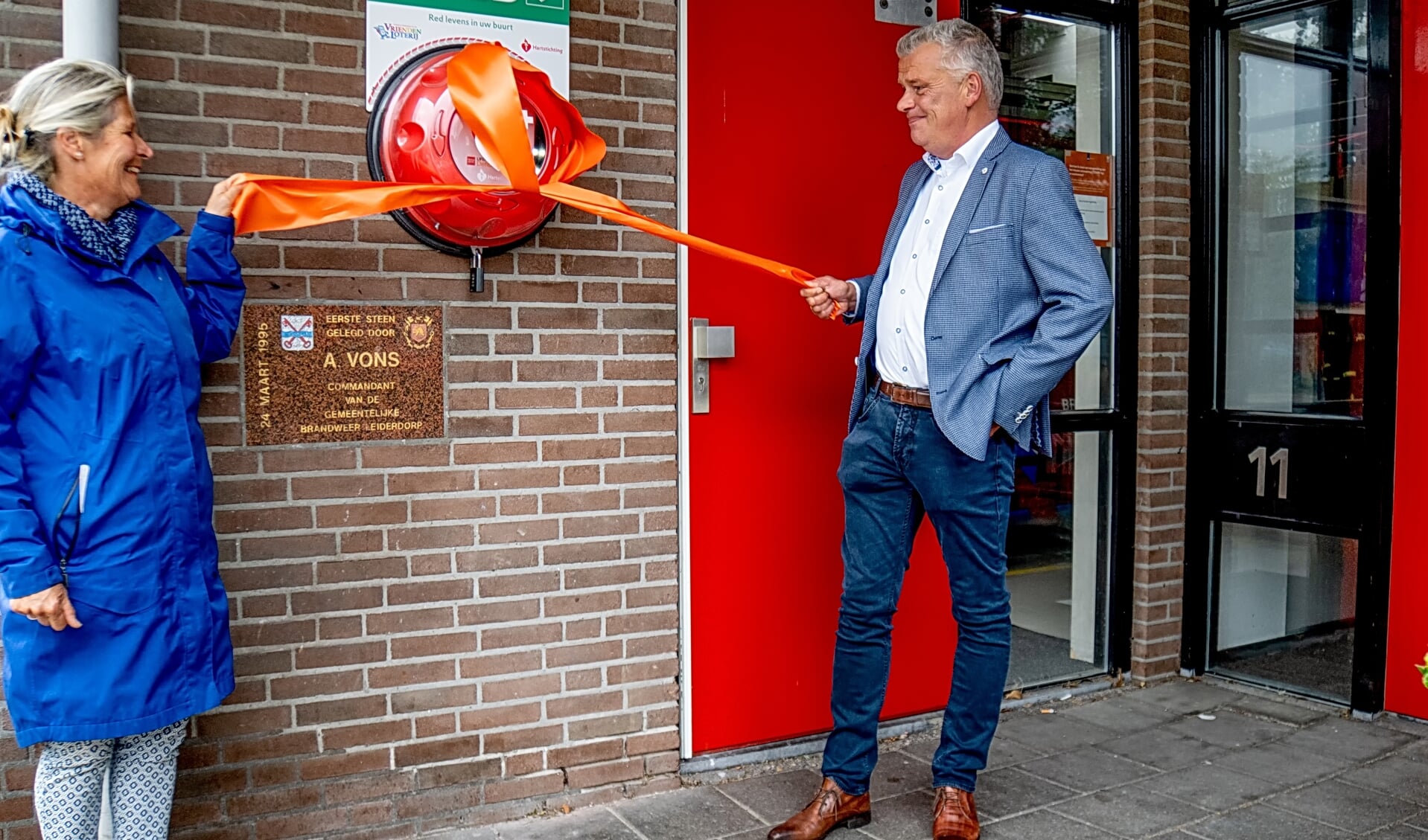 Voorzitter Divera Kapteijn van de EHBO-vereniging Leiderdorp en wethouder Daan Binnendijk openen de nieuwe AED bij de brandweerkazerne.