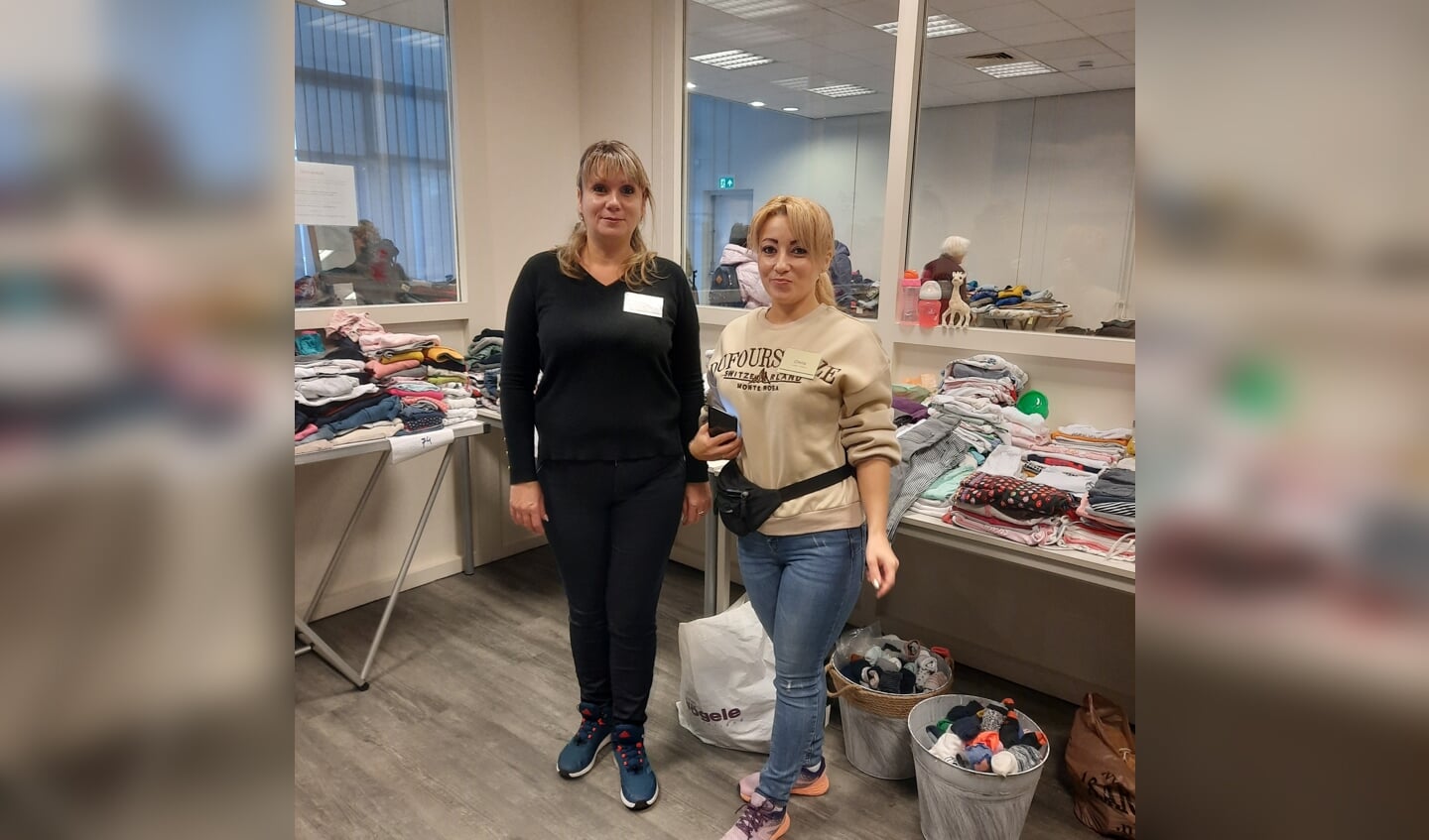 Twee Oekraïense vrijwilligers bij de tafels vol kleding. Hun hulp is van groot belang om de taalbarrière te overkomen. 