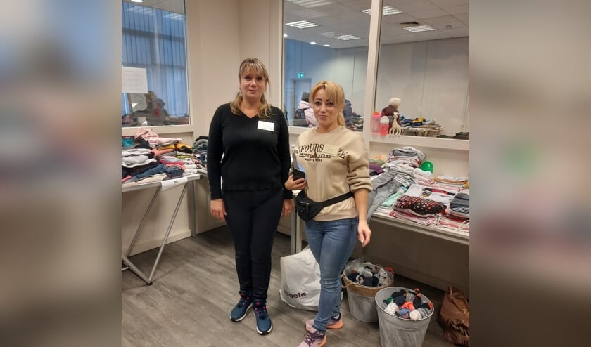 Twee Oekraïense vrijwilligers bij de tafels vol kleding. Hun hulp is van groot belang om de taalbarrière te overkomen. 