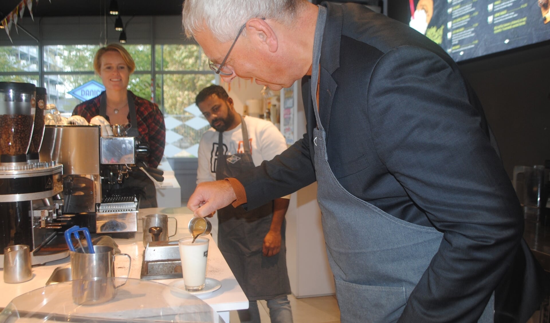 Wethouder Herman Romeijn doet zijn best op een latte macchiato. LOV-voorzitter Lorien de Roode en eigenaar Rudo Slappendel van Danice kijken toe.