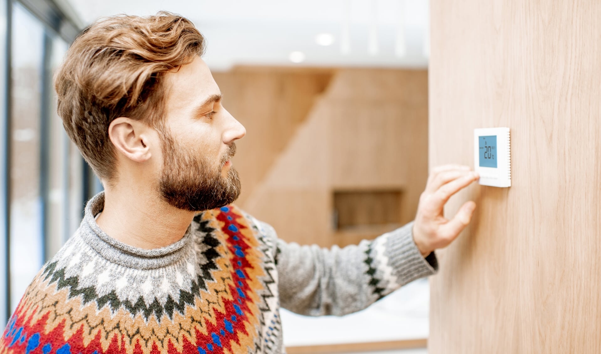 Man in sweater feeling cold adjusting room temperature with electronic thermostat at home