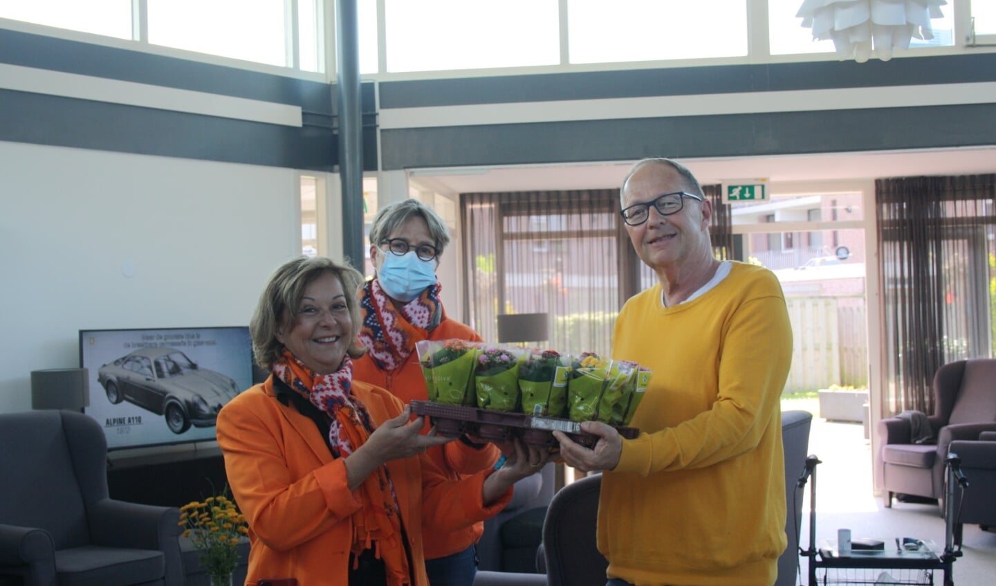 Een van de bewoners neemt de bloemenhulde voor de bewoners van het Jan de Hartogplein in ontvangst van Tineke Zonneveld en Jacqueline Borman van de Oranjevereniging Leiderdorp