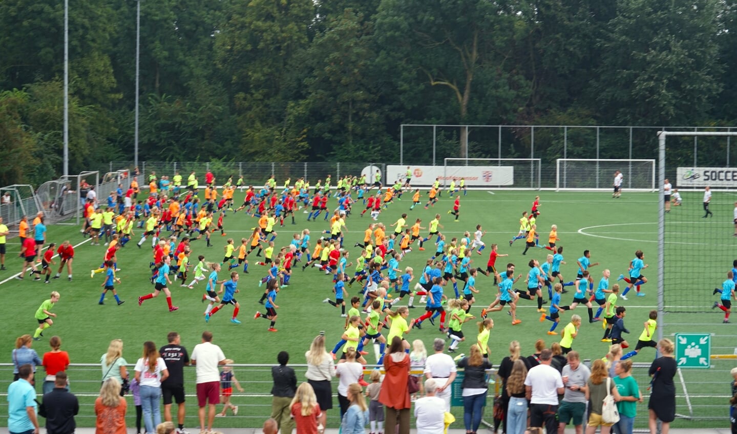 Ouders en vrijwilligers kijken toe bij de warming-up voor de 35ste Voetbalstart.