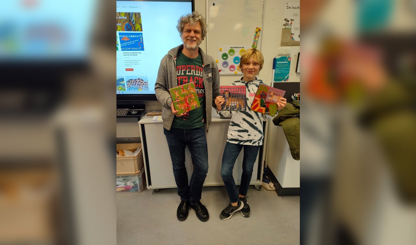 Zachary de Voogd laat samen met jurylid Jeroen Windmeijer de prijs (drie schilderijtjes) aan zijn klasgenootjes zien. | Foto Iris Kruijsdijk