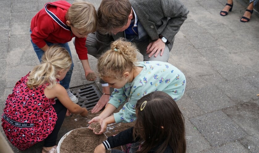 Wethouder Bob Vastenhoud helpt de kleuters een handje bij opvullen van de voegen met zand.