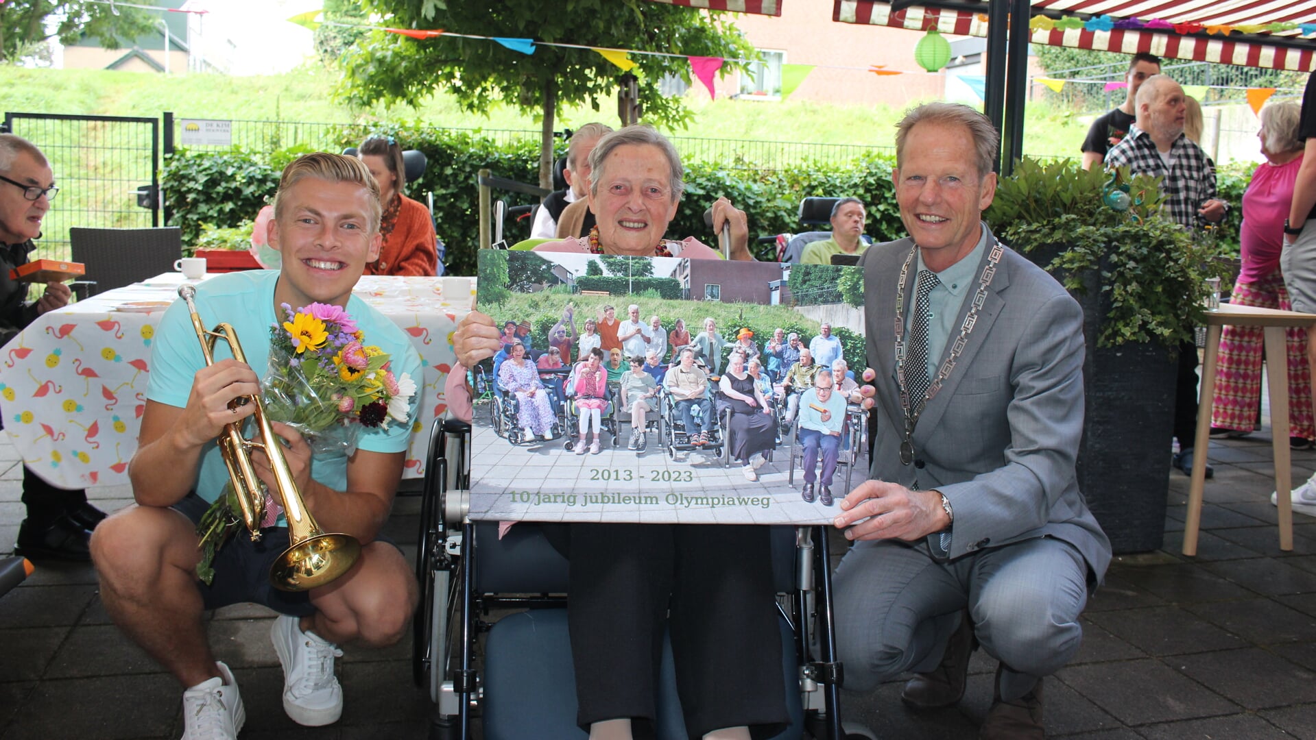 Burgemeester Arie van Erk samen met de oudste bewoonster, de 89-jarige Wil, onthulde een groepsfoto. Links Jeffrey Parmentier. | Foto en tekst: AC