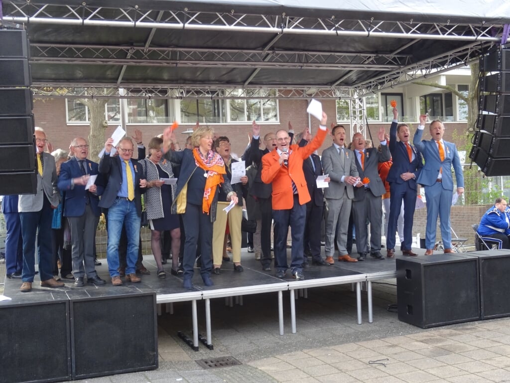 Het podium met gedecoreerden, collegeleden en voorzitter Hans Kruidenberg van de Oranjevereniging heft een driewerf 'hoera' aan voor koning Willem-Alexander.  