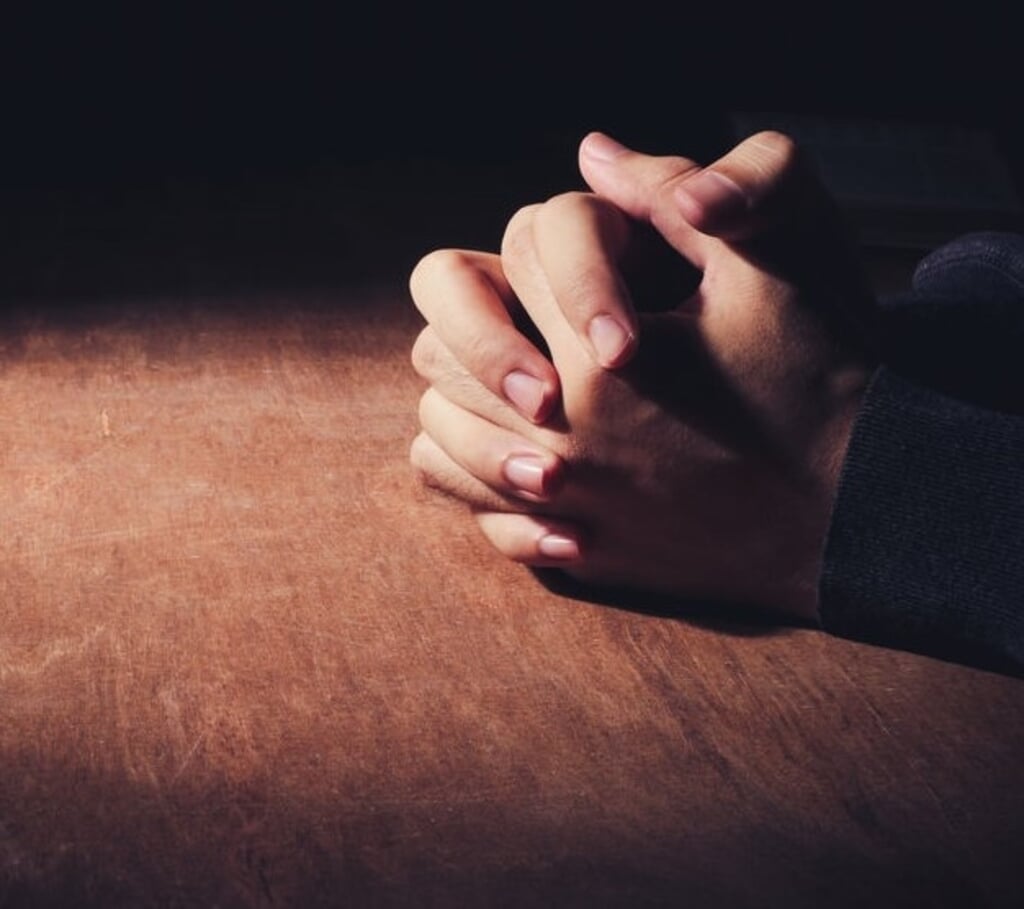 Praying hands of young man on a wooden desk background.