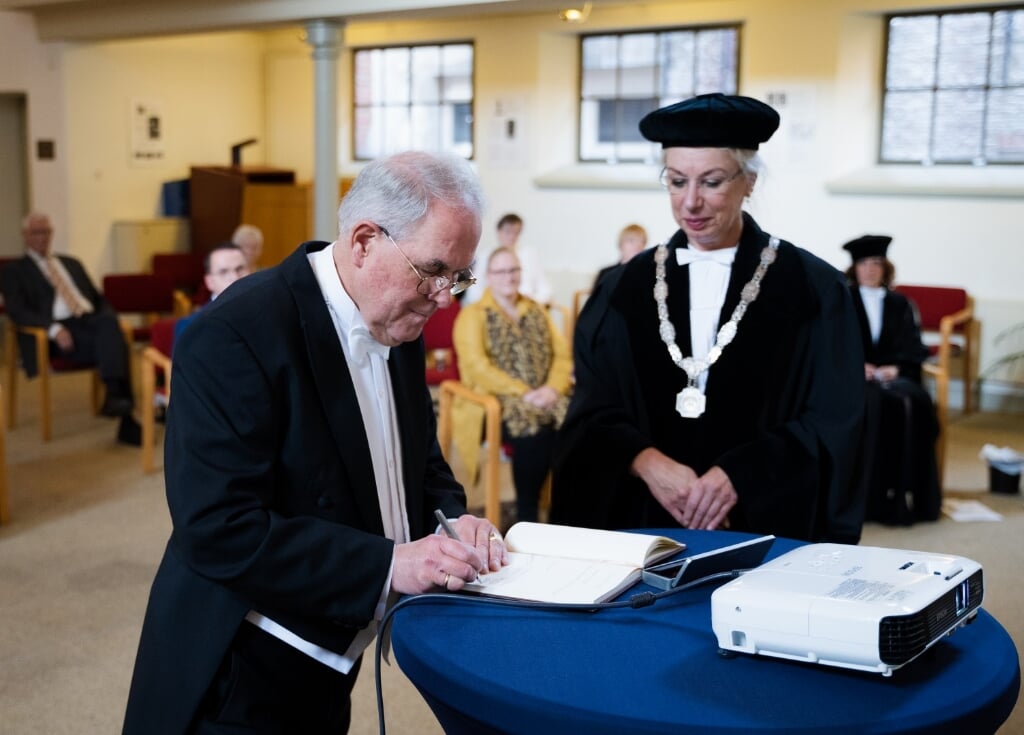 Ds. Weegink zet onder het toeziend oog van de rector prof. dr. Mechteld Jansen zijn naam in het album van mensen die aan de universiteit gepromoveerd zijn. | Foto: pr