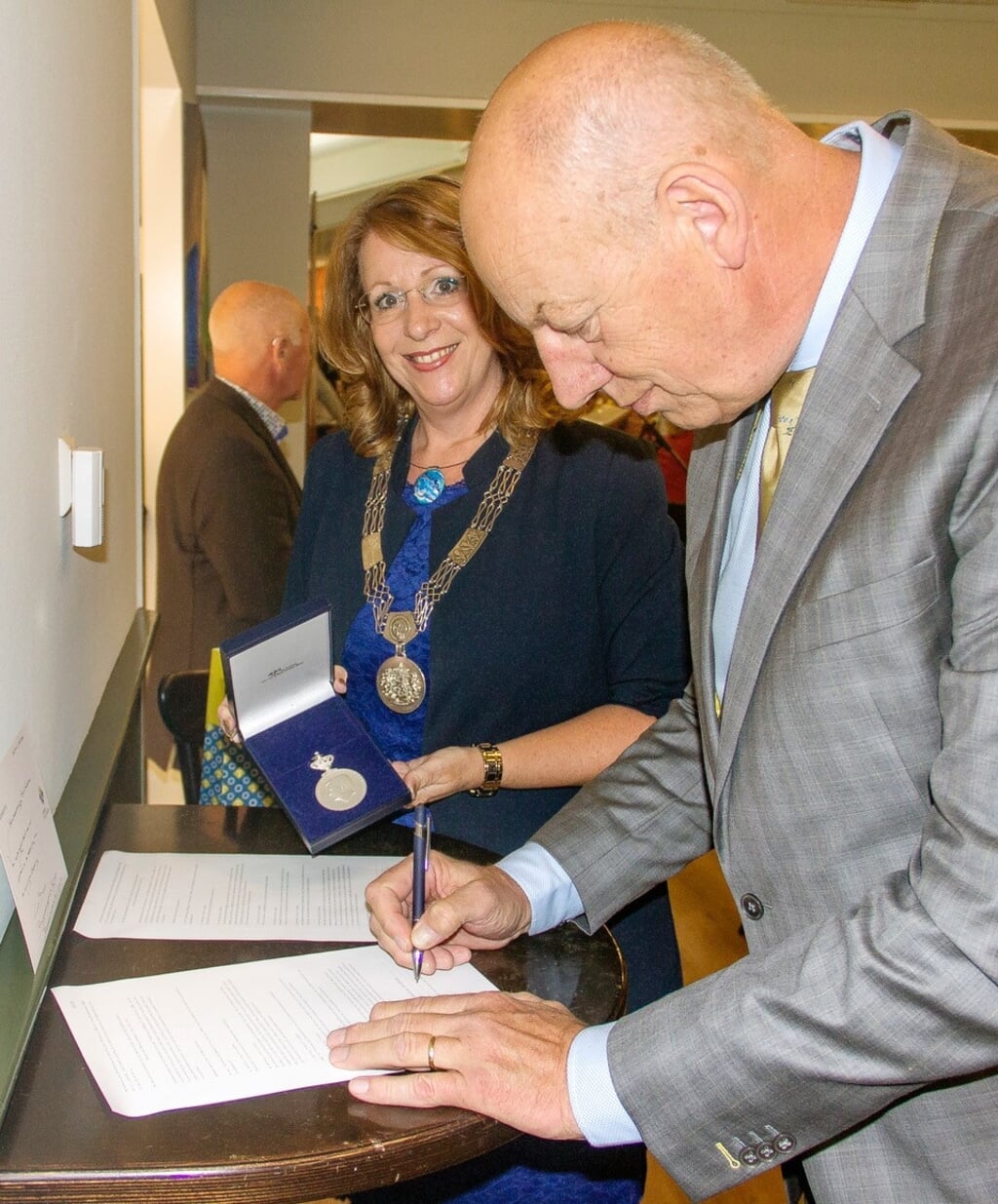 Burgemeester Breuer toont de erepenning. Voorzitter Kees van Velzen ondertekent de papieren. | Foto: pr.