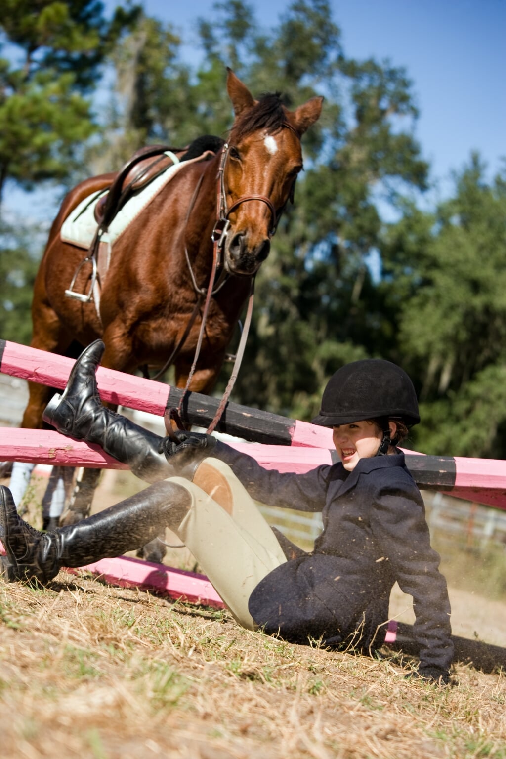Young female equestrian falls off horse while trying to clear an obstacle in competition.