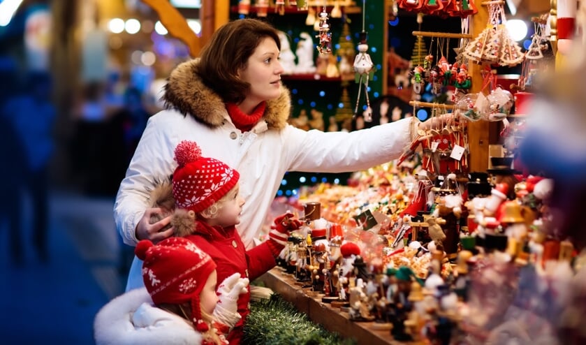 Mother and child in warm hat watching handmade glass Christmas tree ornaments at traditional German Xmas street market. Family with kids shopping for Christmas presents on winter fair on snowy day.