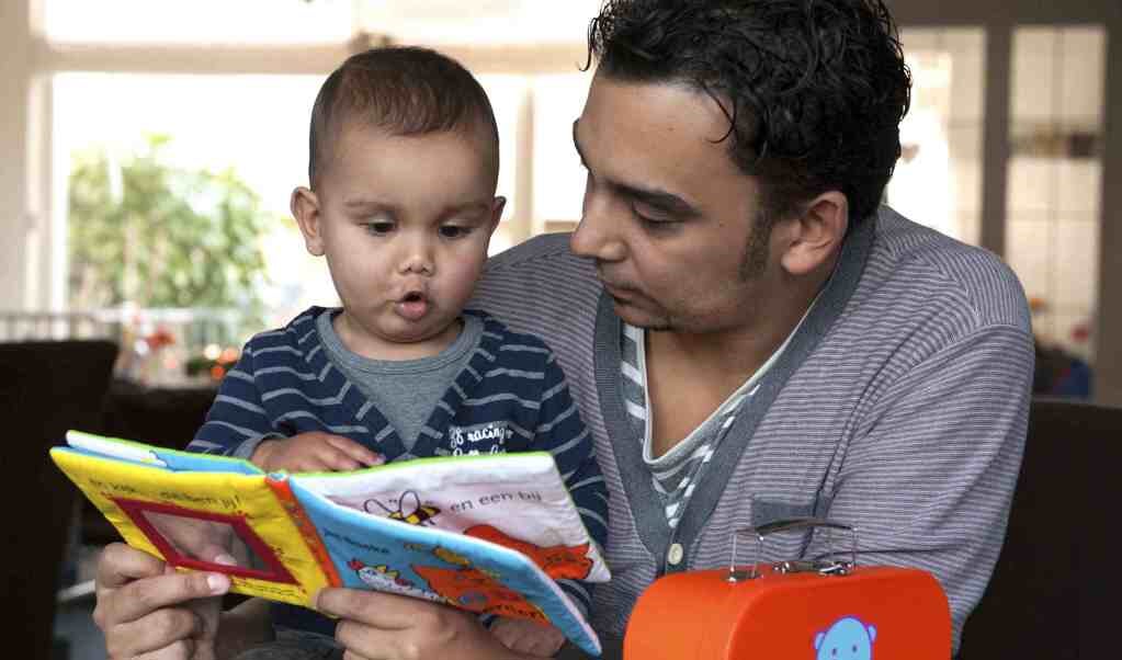 Foto van een vader die een boekje leest met zijn zoontje