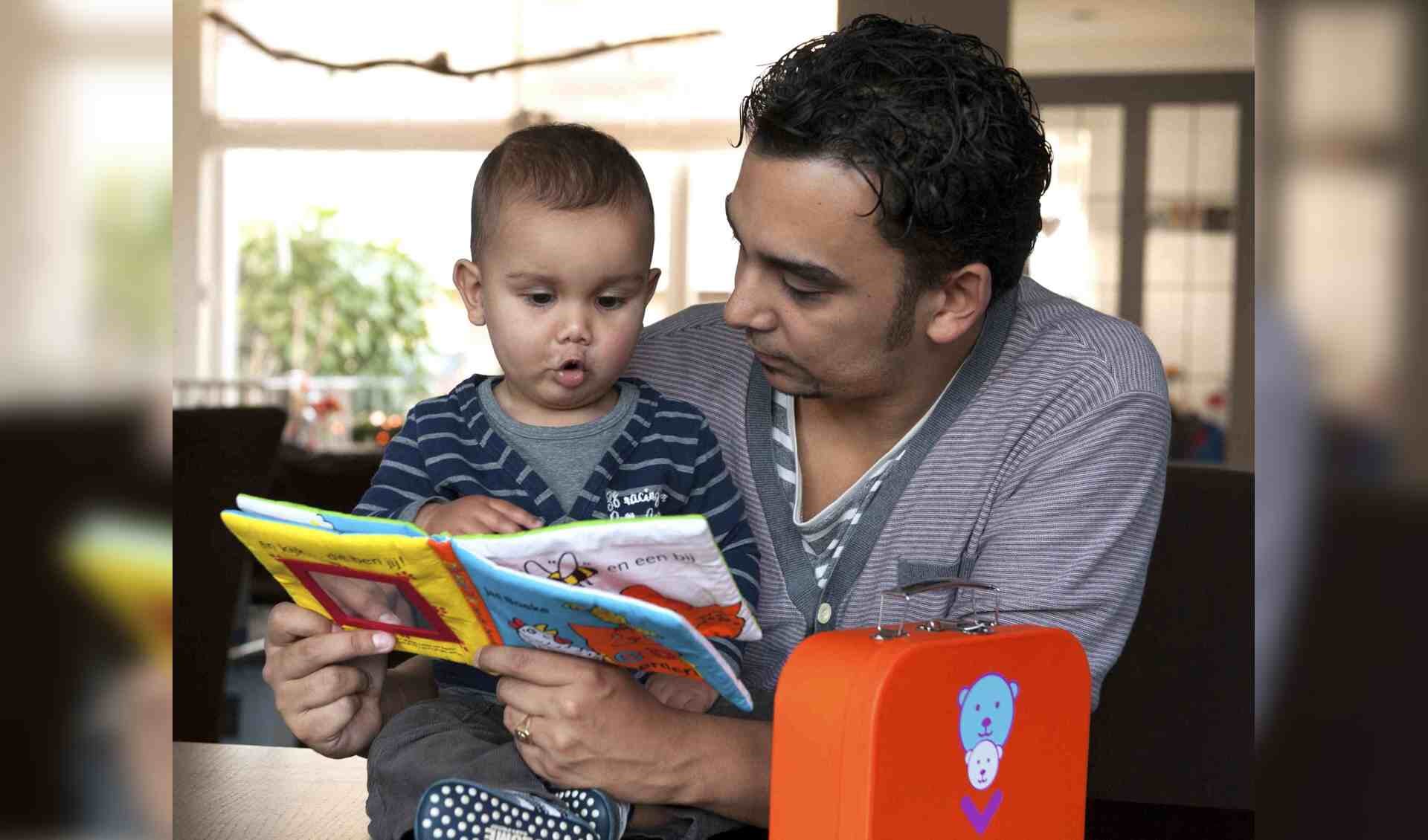 Foto van een vader die een boekje leest met zijn zoontje