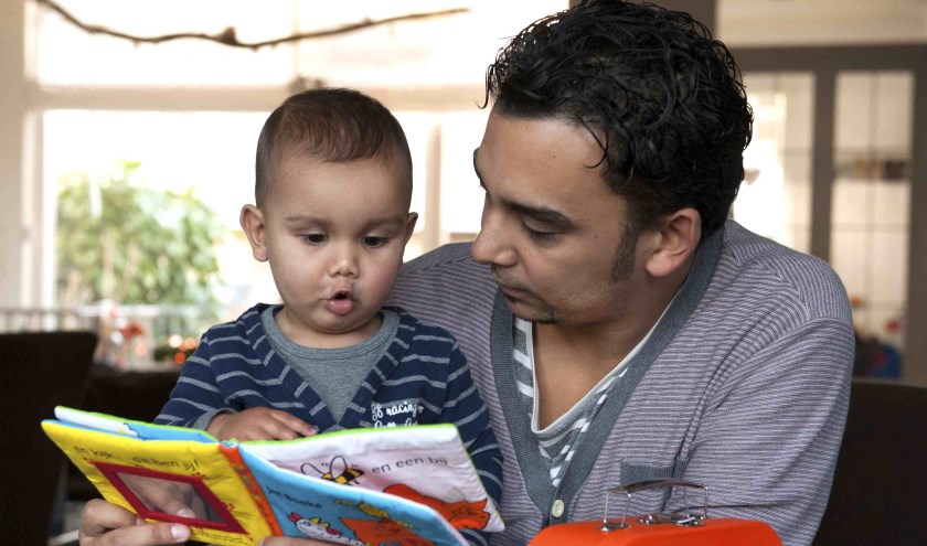 Foto van een vader die een boekje leest met zijn zoontje